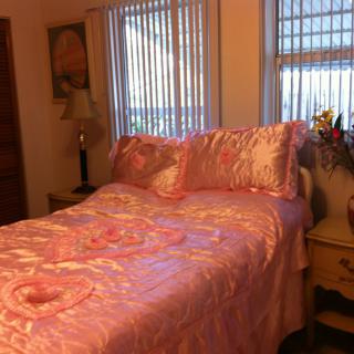 A cozy bedroom featuring a bed with pink bedding and decorative pillows, next to a window with blinds.