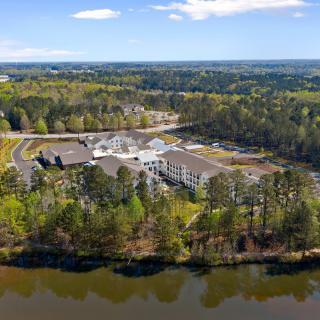 Aerial view of a large building surrounded by forest and near a lake.