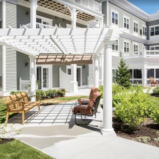 A beautiful patio area with a pergola, benches, and lush landscaping outside a residential building.