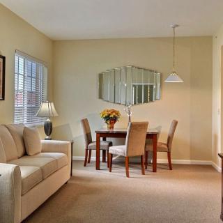A cozy living room with a dining area featuring a sofa, table with chairs, and a decorative mirror on the wall.