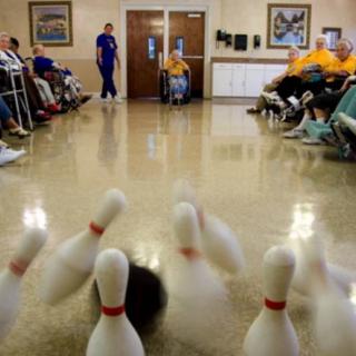 Elderly residents engage in a lively indoor bowling game at a nursing home.