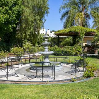 A serene outdoor garden area featuring a central fountain surrounded by chairs and lush greenery.