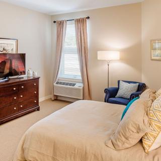 A cozy bedroom with a neatly made bed, dresser, and an armchair by the window.