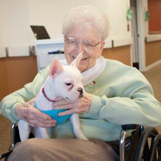 An elderly woman sitting in a wheelchair holding a small puppy indoors.