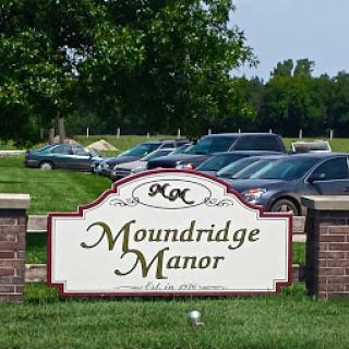 Entrance sign of Moundridge Manor with parked cars in the background.