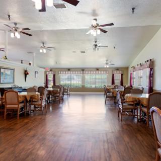 A spacious dining area with wooden floors and multiple ceiling fans, furnished with several tables and chairs.