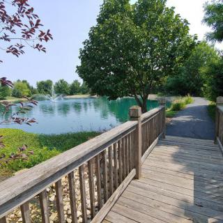 A serene pathway leading over a wooden bridge beside a tranquil lake surrounded by lush greenery.