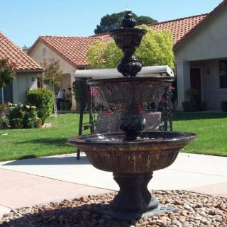 A two-tiered fountain in a garden setting with houses and a well-maintained lawn.