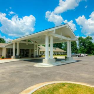 A building with a covered entrance and driveway, set against a partly cloudy sky.