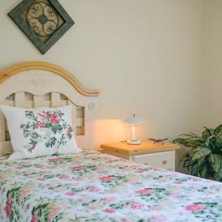 A cozy bedroom with a single bed featuring floral bedding, accompanied by a nightstand and a lamp.
