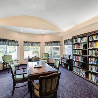 A cozy library room with bookshelves, a meeting table, and several chairs.