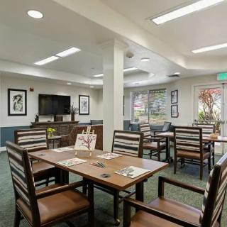 A modern dining area with wooden tables and chairs, featuring large windows and bright lighting.