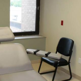 An examination room featuring an examination table and a chair near a window.