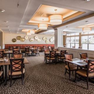 A spacious, elegantly designed restaurant dining area with neatly arranged tables and chairs, featuring stylish chandeliers and a patterned carpet.