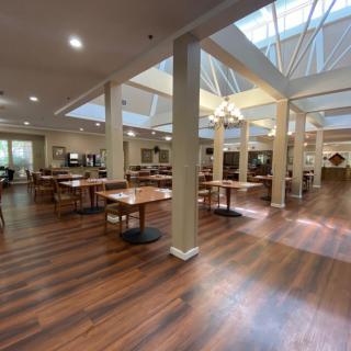 An empty dining area with wooden floors and skylights, featuring tables and chairs arranged neatly.