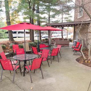 A cozy patio with red chairs and umbrellas, surrounded by trees and adjacent to a building.