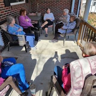 A group of seniors enjoying a sunny day together on the porch, engaged in conversation.