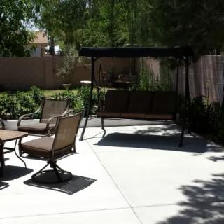 A sunny backyard patio with a swing chair, chairs, and a table.