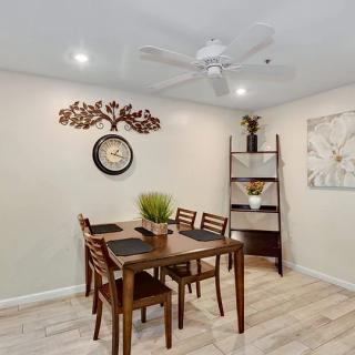 A cozy dining room featuring a wooden table with chairs, decorated with a wall clock, artwork, and a shelf with plants.