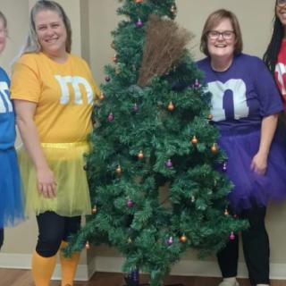 A group of people dressed in colorful costumes posing by a decorated tree.