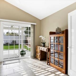A bright and cozy living room with sliding glass doors, featuring a wooden cabinet and desk, enhanced by natural lighting.