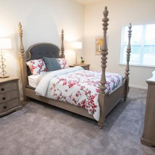 A cozy bedroom featuring a four-poster bed with floral bedding, complemented by two nightstands and table lamps, on a carpeted floor.