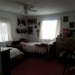A cozy bedroom with twin beds, decorated with wall art and illuminated by natural light from two windows.