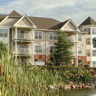 A peaceful residential apartment building overlooking a small lake surrounded by trees and plants.