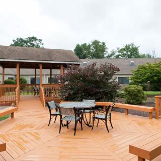An outdoor deck area featuring a central table with chairs, surrounded by lush greenery and a gazebo.