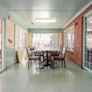 A cozy indoor dining area with a table and chairs, surrounded by windows and a brick wall.