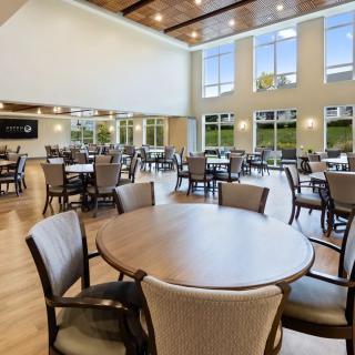 A spacious dining area with multiple tables and chairs, featuring large windows and wooden flooring.