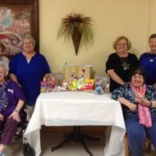 A group of women posing together indoors with a table displaying various items.
