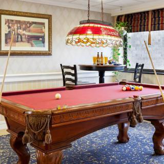 A cozy game room featuring a red felt pool table with two cues and an ornate hanging light.