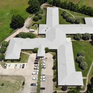 Aerial view of a large building complex with a parking lot and surrounding greenery.