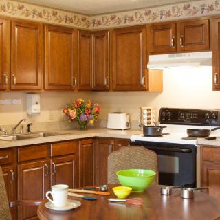 A cozy kitchen with wooden cabinets, a stovetop, and a dining table set with dishes.
