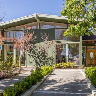 A modern mid-century style home with large windows and lush landscaping.