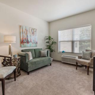A cozy living room with a green sofa, armchairs, and a large window allowing natural light.