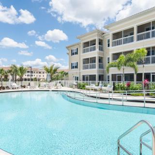A modern residential complex with a large swimming pool surrounded by palm trees.