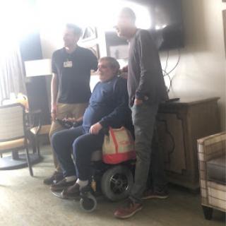 A group of friends posing together indoors, with one person in a wheelchair.