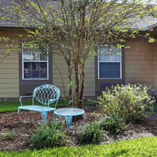 A garden with a turquoise bench and table surrounded by shrubs and a tree.
