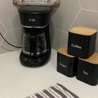 A kitchen countertop with a coffee maker and labeled canisters for coffee, sugar, and tea.