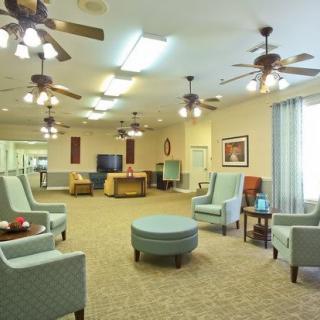 A spacious living room with multiple seating areas, ceiling fans, and warm lighting.