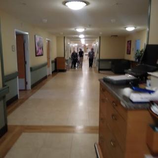 A view of a hospital corridor, featuring a reception area and patients walking in the distance.