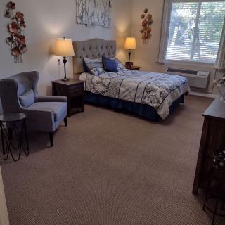 A cozy bedroom with a bed, chair, and bedside lamps, featuring wall decor and a large window.