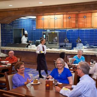 A group of people enjoying a meal at a restaurant with visible kitchen staff in the background.