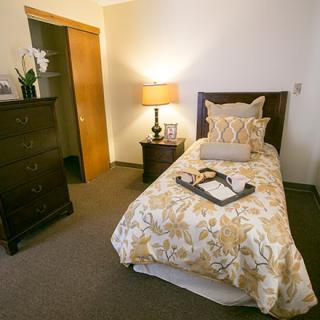 A cozy bedroom with a single bed adorned with decorative pillows next to a side table and lamp.