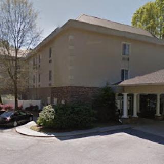 A view of a hotel with a parking area and surrounding trees.