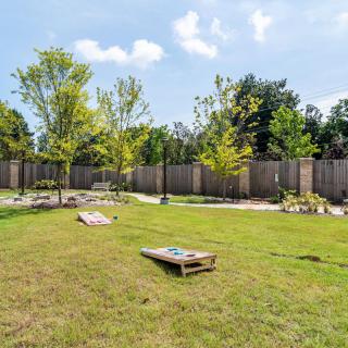A backyard with cornhole boards set up on the grass, surrounded by trees and a wooden fence.