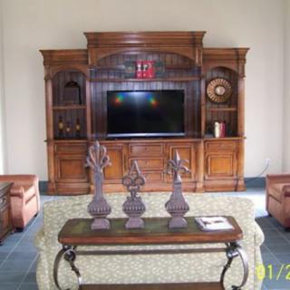 A living room setup featuring a large wooden entertainment center with a television, decorative statues on a table, and comfortable sofas.