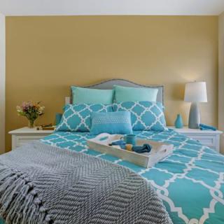A cozy bedroom with a turquoise and white color scheme, featuring a neatly arranged bed, decorative pillows, and a bedside lamp.